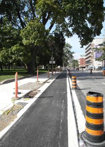 The almost-completed separated cycle path on Sherbourne St at Gerrard. The rounded mountable kerb is in the far background. The squared kerb begins at the accessible bus stop (rectanglar gravel patch in the left centre of the photo).