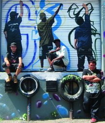 At right, Jared VanderReest, Jessey Pacho, and Jasper Urbina pose in front of their own images at Youthlink InnerCity. The mural was painted as part of a program that Adam Vaughan describes as “a testament to the depth of talent of Toronto youth, to the